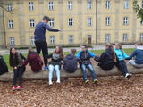 Jugendliche sitzen auf einem Baumstamm. Ein Teilnehmer versucht über diese hinwegzusteigen.