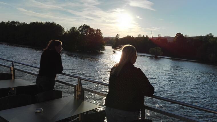 zwei junge Damen schauen bei der Zeichenhandlung des Gottesdienstes auf die Donau Richtung Sonnenuntergang