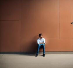 Junger Mann sitzt alleine vor einer Wand