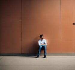 Junger Mann sitzt alleine vor einer Wand