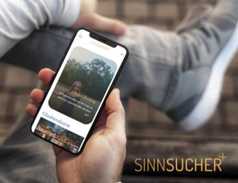 Junge hält Handy auf diesem ist die Startseite von sinnsucher+ zu sehen