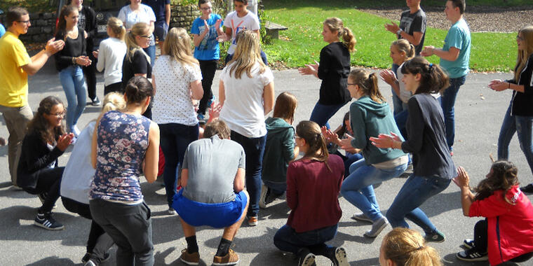 Jugendliche spielen ein Gruppenspiel. Sie stehen auf einem Parkplatz und sprechen miteinander.