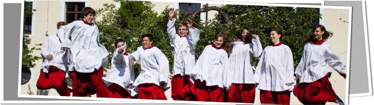 Ministrantinnen und Ministranten im Roten Talar und Chorrock auf einer grünen Wiese springend.